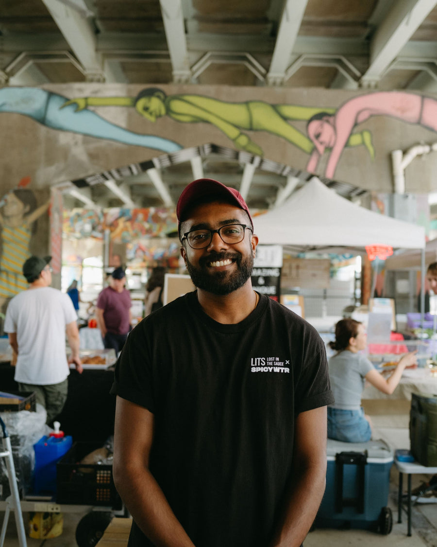 Founder of Lost in the Sauce, Karthy Subramaniam, standing in front of the LITS booth at the Underpass market in Toronto.