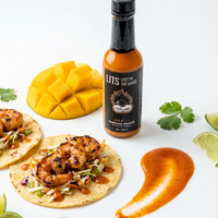 Burning Mango mango habanero hot sauce bottle with grilled shrimp tacos, sliced mango, lime and cilantro (hover), photo 3